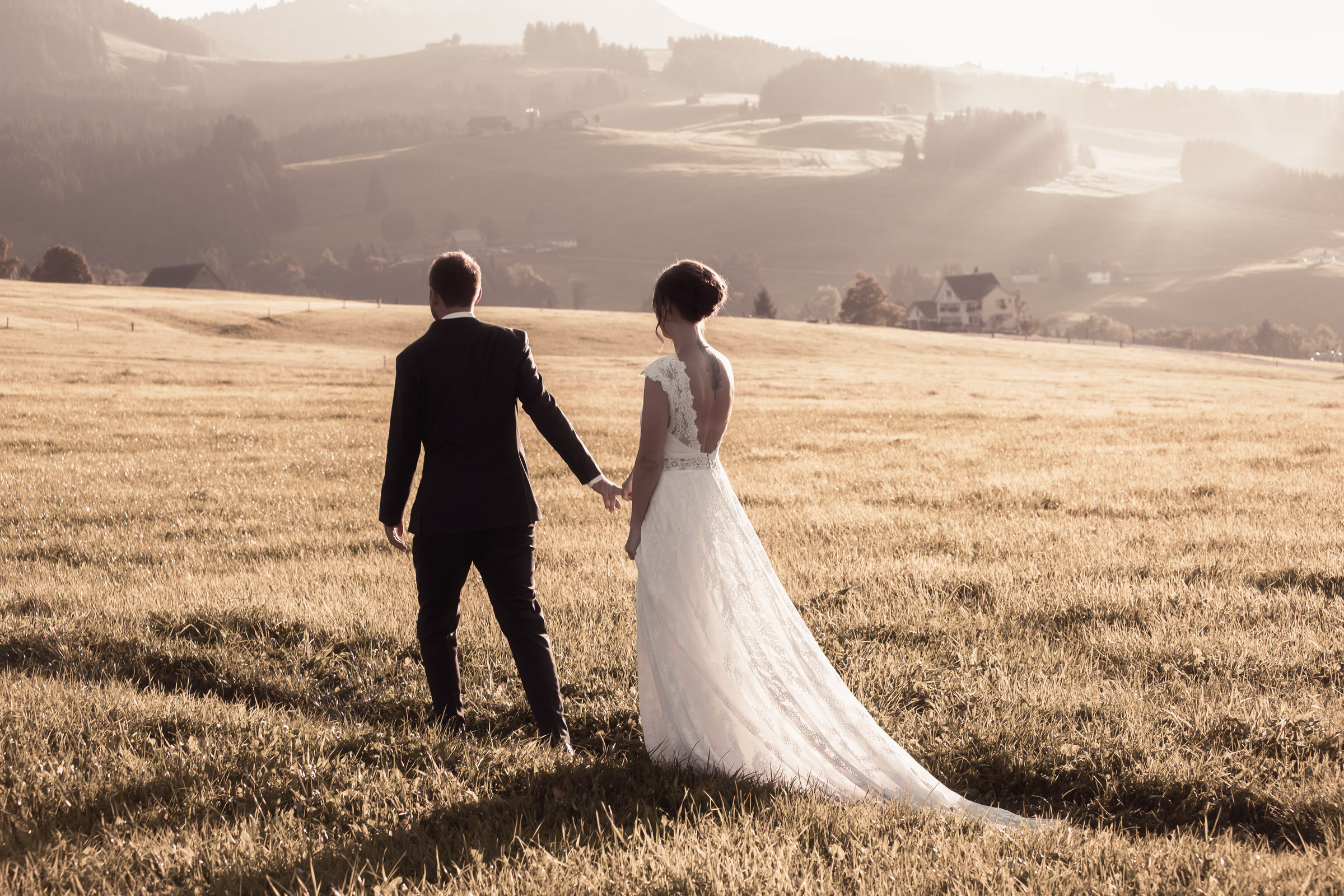 Der Fotograf Franco Baumann: Hochzeitspaar geht über eine grosse Wiese, die Sonne strahlt, aufgenommen für die Rubrik Hochzeit in St. Gallen und Toggenburg.